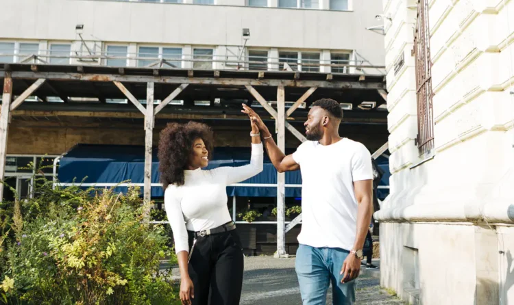 High five between a smiling young couple outside an urban building, symbolizing successful property investment and real estate opportunities in Tanzania.